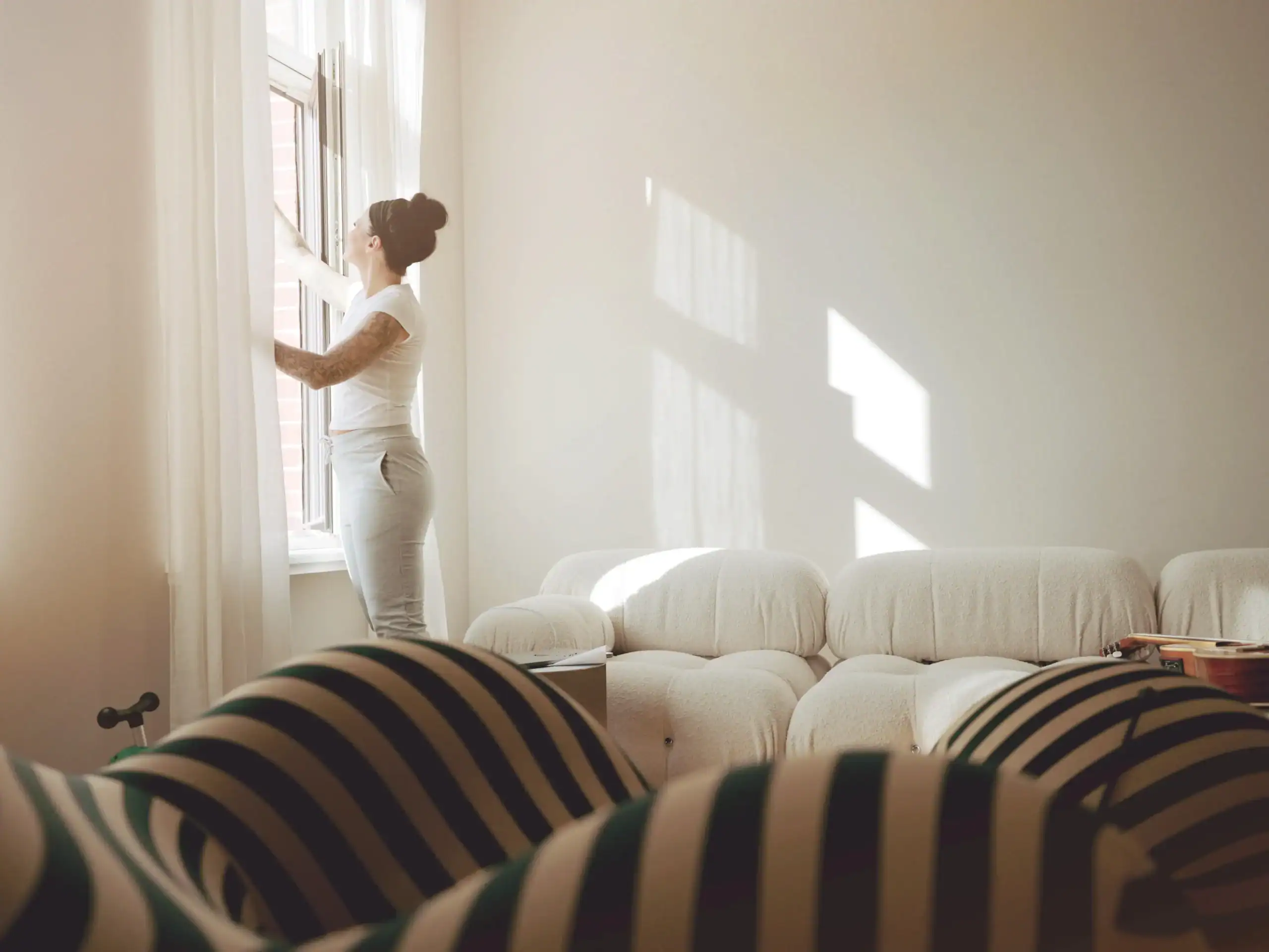 Frau schaut durch das Fenster in einem hellen Wohnzimmer.